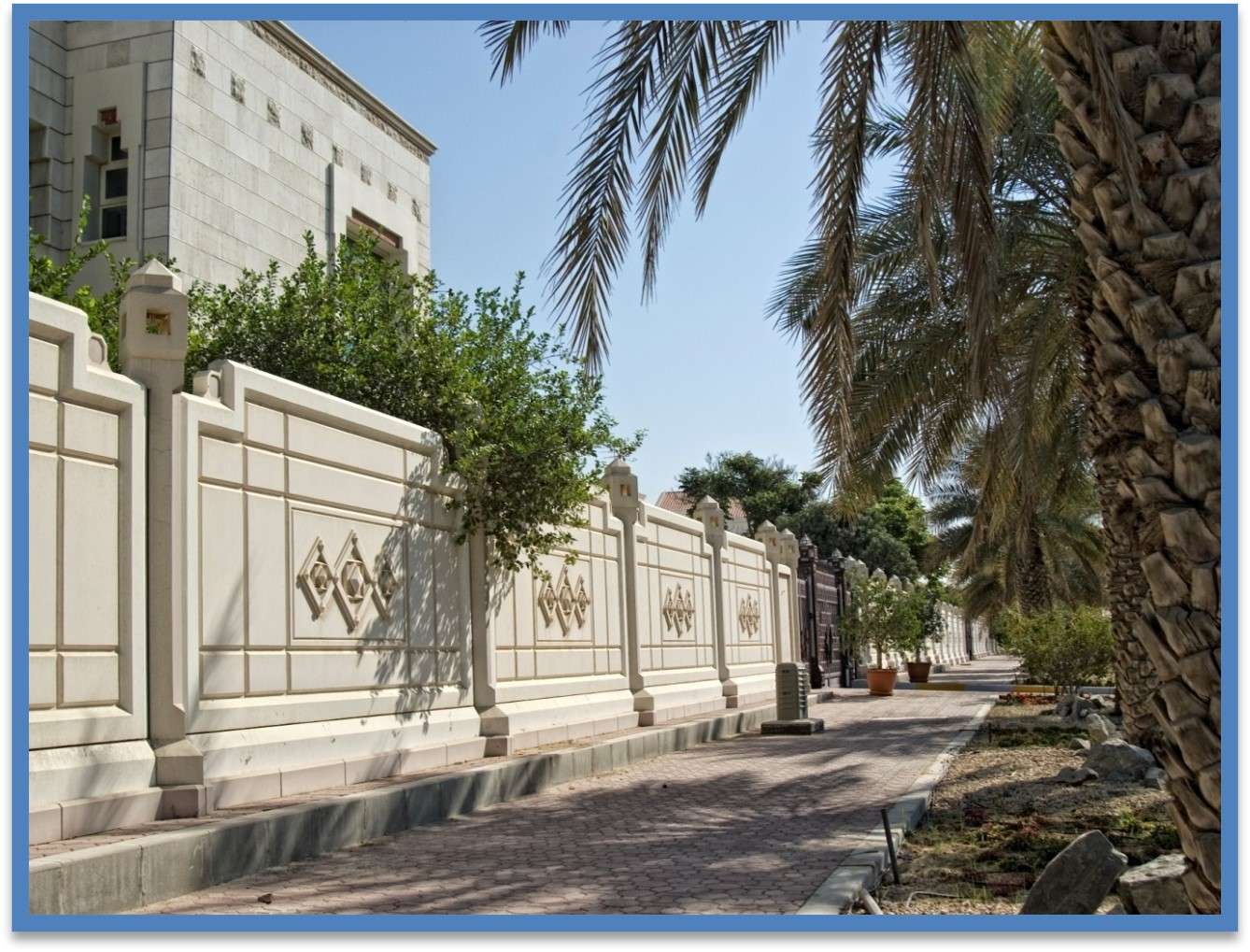 Bw1 White precast boundary wall with diamond relief patterns and decorative pillars along palm tree-lined sidewalk